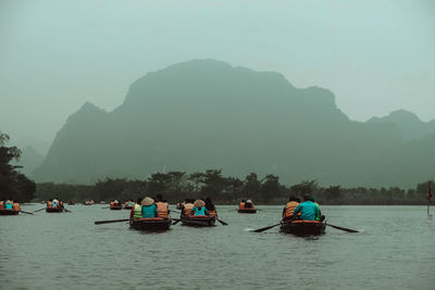 People kayaking on lake against mountains