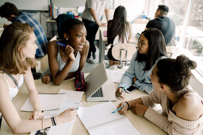 Teenage girls discussing while sitting by table in classroom