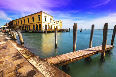 Wooden posts in canal by building against sky