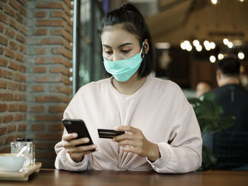 Young woman using smart phone on table at window