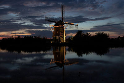 Traditional windmill by lake against sky during sunset