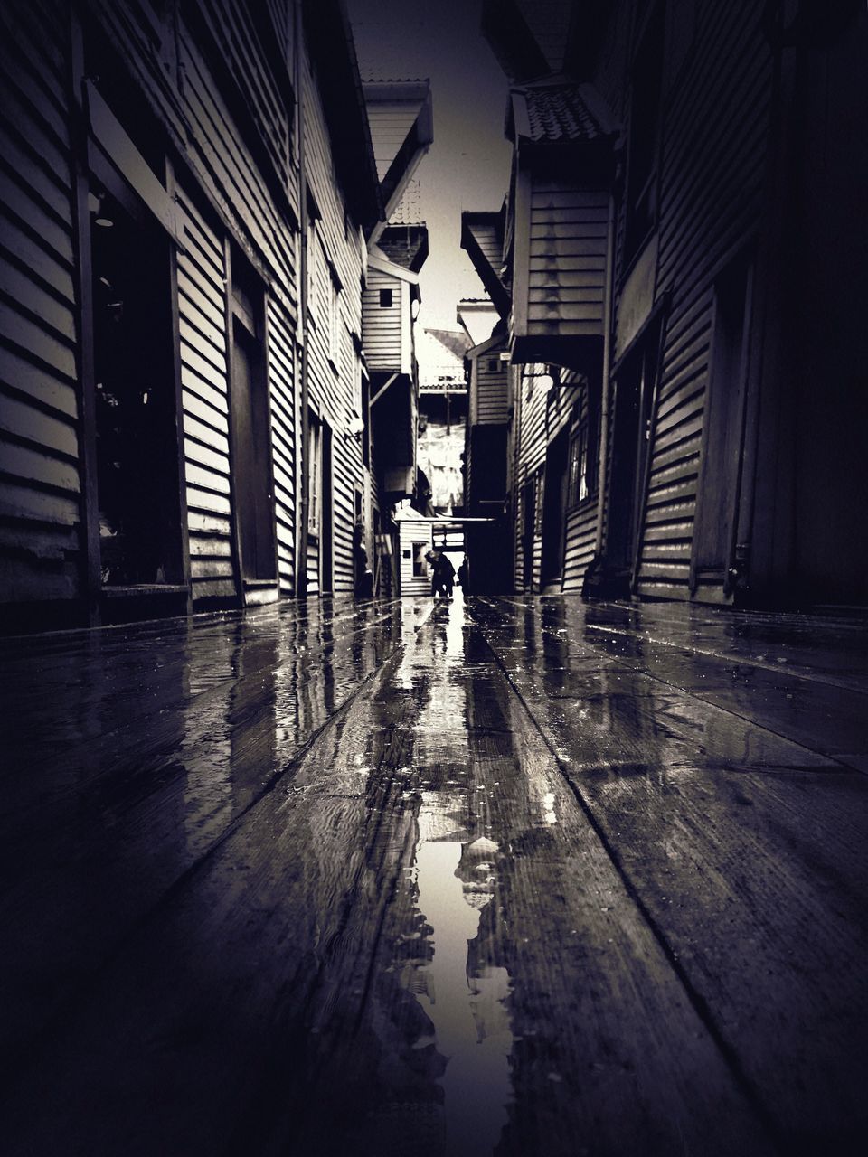 PEOPLE WALKING ON WET STREET AMIDST BUILDINGS IN CITY