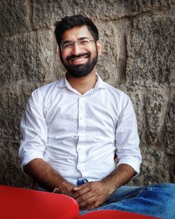 Portrait of a smiling young man sitting against wall