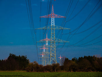 Low angle view of electricity pylons on field against blue sky