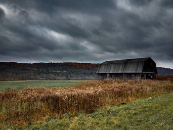 Abandoned house on field against storm clouds