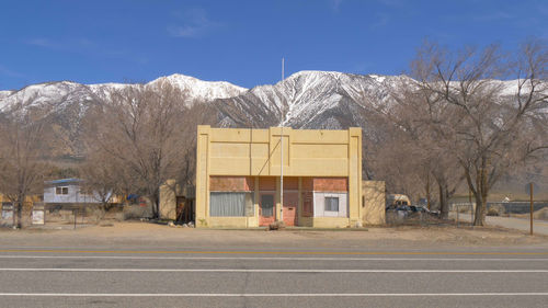 Road by bare trees and buildings against sky