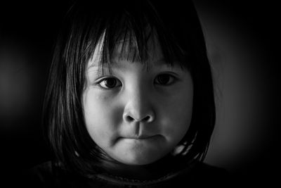 Close-up portrait of cute girl against black background