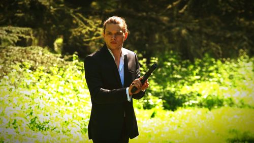 Portrait of young man holding hand gun at field