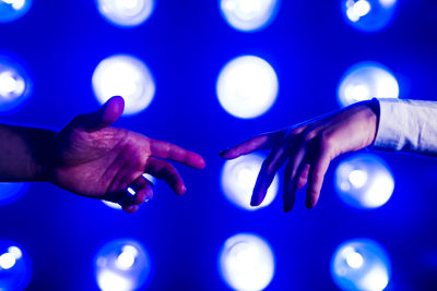 Hands of couple reaching towards each other in front of illuminated lights