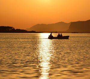 Silhouette people sailing on boat in river against clear sky during sunset