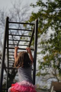 Girl climbing on monkey bars against sky