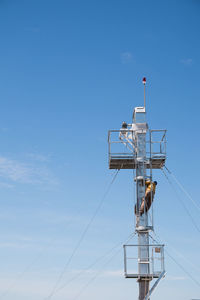 Low angle view of people working on tower against blue sky