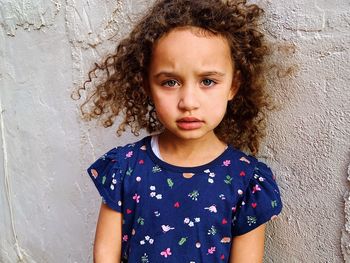 Portrait of girl with curly hair standing against wall