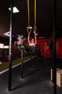 Muscular female athlete in sportswear hanging on gymnastic rings and doing exercises for abs in contemporary fitness center