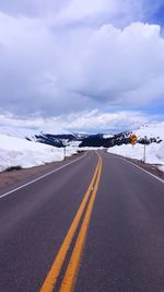 Empty road leading towards snowcapped mountains against cloudy sky