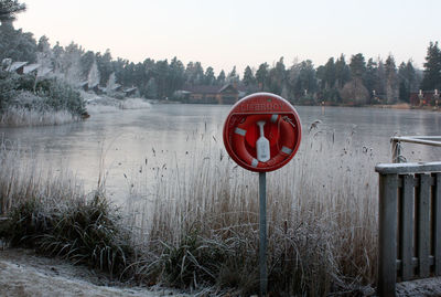 Information sign on wooden post by lake against sky