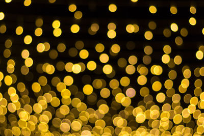 Defocused image of illuminated golden christmas lights against black background