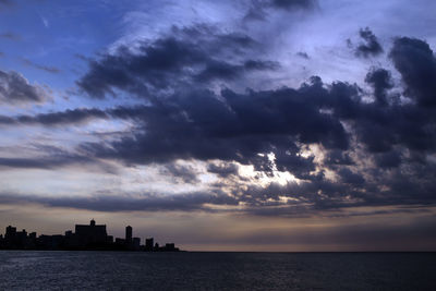 Silhouette of city at waterfront against cloudy sky