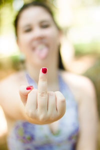 Portrait of confident young woman showing middle finger while sitting at park