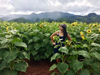 Woman standing amidst sunflowers on field against mountain