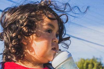 Close-up of cute boy drinking milk against sky