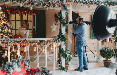 Full length of man photographing young woman through camera at home during christmas