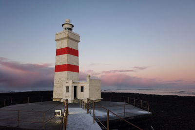 Lighthouse by sea against sky during sunset