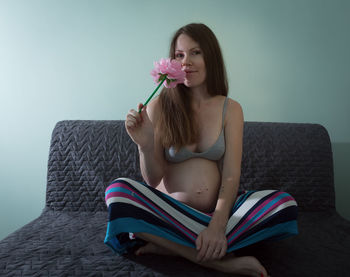 Portrait of woman smelling flower while sitting on sofa in living room at home