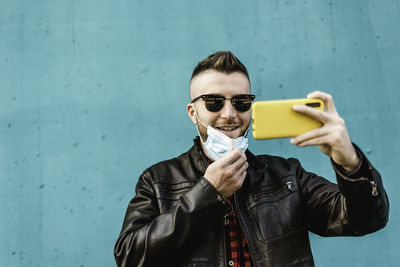 Smiling man wearing mask doing selfie against wall