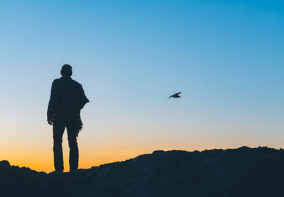 Rear view of silhouette man standing against sky during sunset