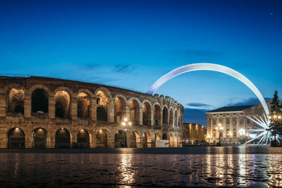 Arch bridge over river against buildings at night