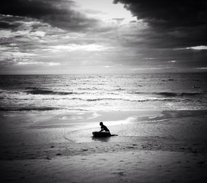 Silhouette man surfboarding in sea against cloudy sky