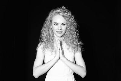 Portrait of woman with hands clasped against black background