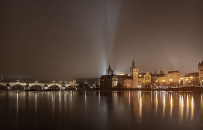 Illuminated city by river against sky at night