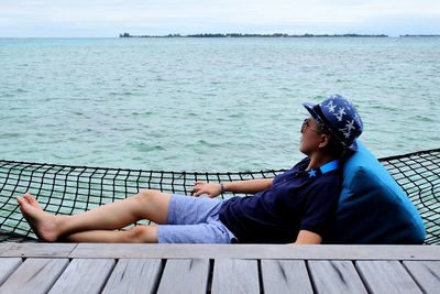 Woman relaxing on hammock by pier over sea