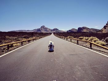 Rear view of woman sitting on road amidst land