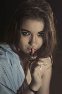 High angle portrait of beautiful woman with finger on lips against black background