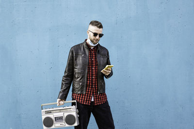 Young man wearing sunglasses standing against wall