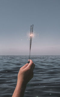 Person hand holding umbrella at sea shore against sky