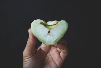 Close-up of hand holding apple against black background