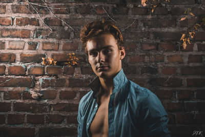 Portrait of young man standing against brick wall