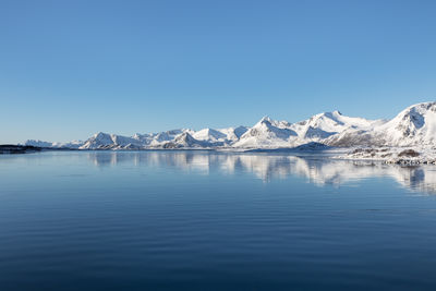 Scenic view of lake by snowcapped mountains against clear blue sky