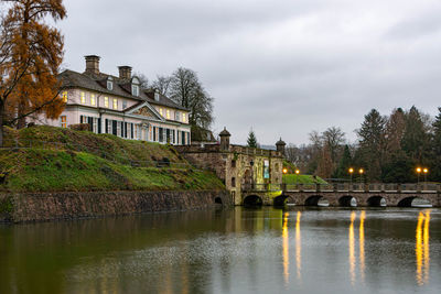 Arch bridge over river by buildings against sky