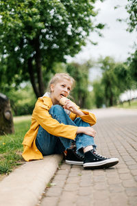 Boy looking away while sitting on plant against trees