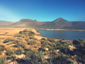 Scenic view of lake and mountains against clear blue sky