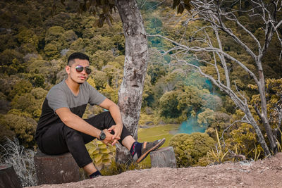 Young man sitting on rock against trees