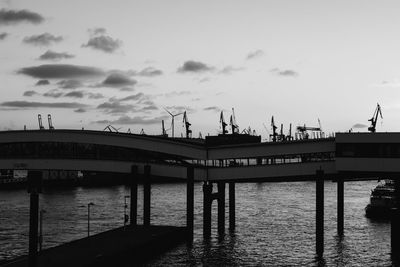 Pier over sea by commercial dock against sky