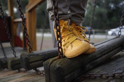 Close-up of person wearing yellow shoes while standing on wood at playground