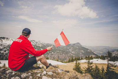 Rear view of man sitting on mountain against sky