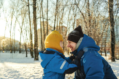 Side view of smiling father and son looking at each other during winter